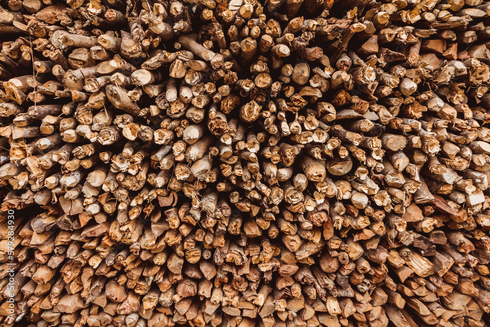 Close up on a pile of chopped wood for burning, with round logs and wedge timber stacked to form a background