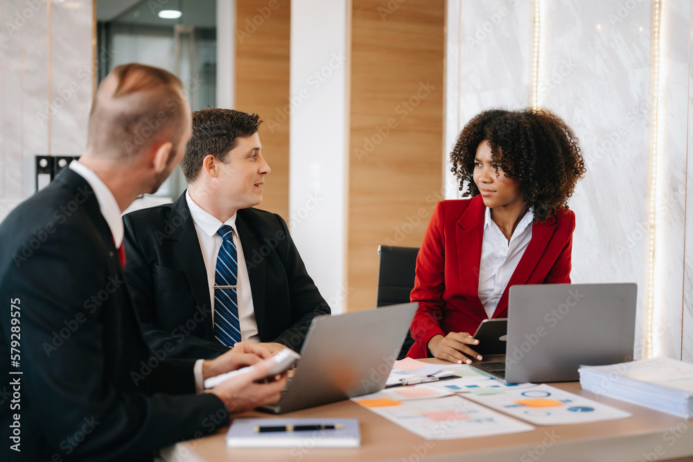 Happy businesspeople while collaborating on a new project in an office. Group of diverse businesspeople using a laptop and tablet in office.. Happy businesspeople while collaborating on a new project in an office. Group of diverse businesspeople using a laptop and tablet in office..
