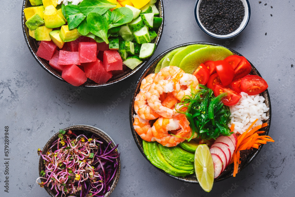 Poke bowl set with  tuna, salmon, shrimp with avocado, mango, radish, rice and other ingredients. Soy sauce and sesame dressing. Gray table background, top view