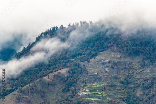 A Himalayan village with terraced fields on the slopes of a hill covered in mist and fog in Kumaon, Uttarakhand. © Balaji