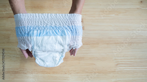 Young mother hands holding white baby diaper pants on light woodle table background.