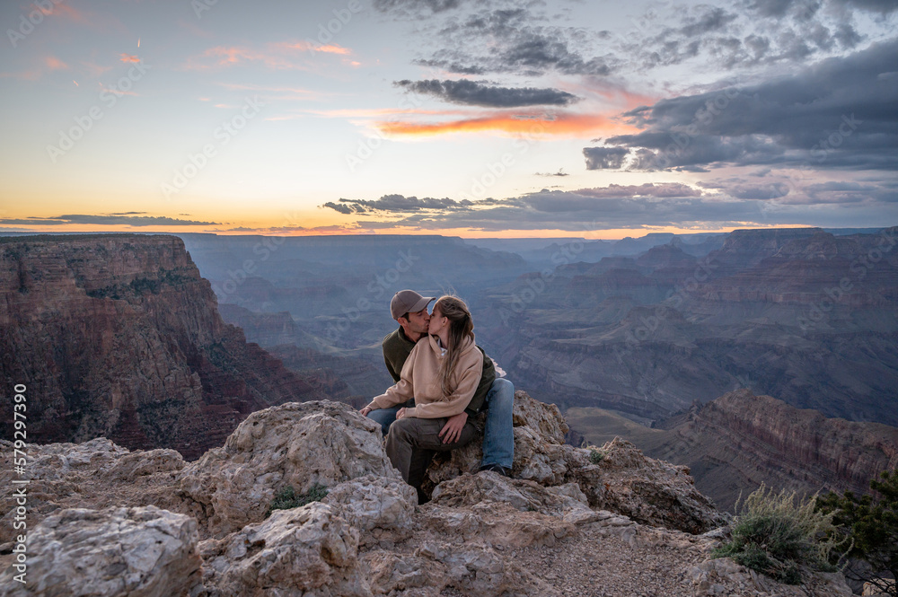 Young wedding couple kissing sitting on the rock of the precipice of the grand canyon at sunset
