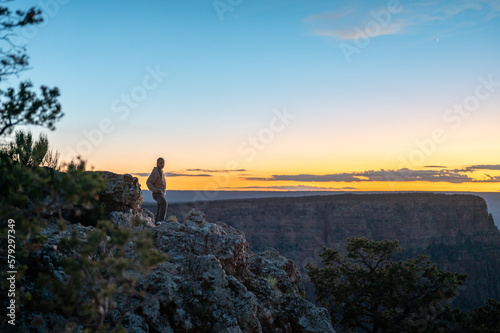 Silhouette of a young adventurer on the edge of the precipice of the Grand Canyon at night sunset