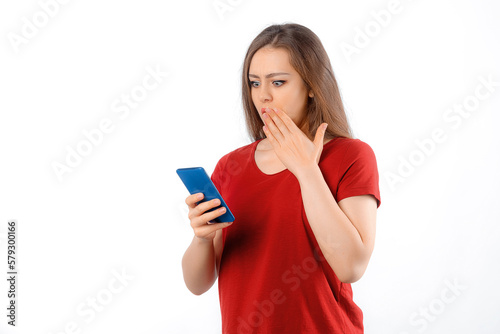 Portrait of lovely young woman using mobile phone, texting message, watching on smartphone, looking impressed with disbelief, standing over white background