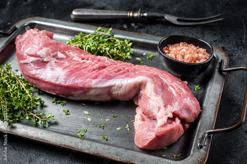 Raw pork tenderloin fillet meat in steel tray with herbs. Black background. Top view