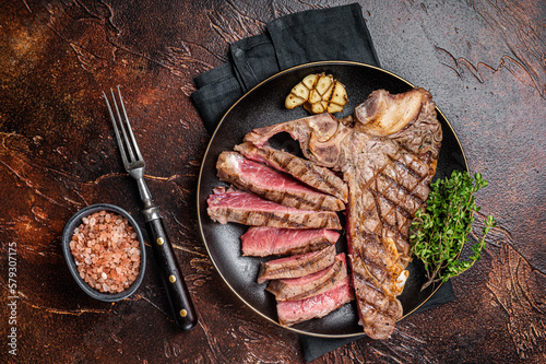 Grilled Medium rare Porterhouse, T-Bone Steak sliced in a plate. Dark background. Top view
