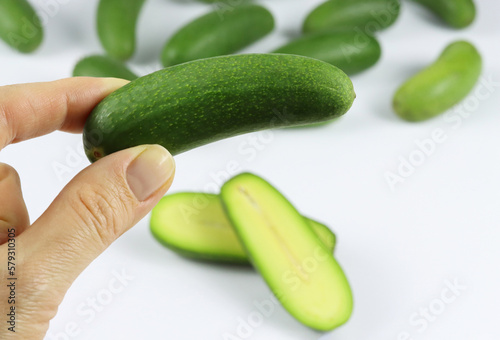 Close up of a hand holding mini avocado with a group of cocktail avocado on the back isolated on white. Specially cultivated exotic green vegan food for healthy living. Functional food or a superfood