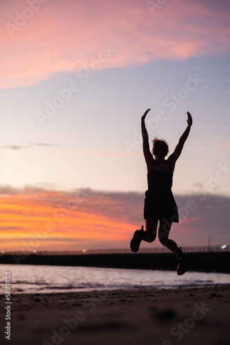 A young girl admires the sunset on the ocean, enjoys life, arms outstretched to the sides, rear view.