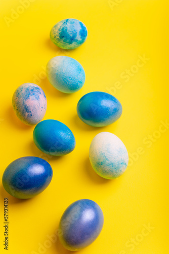 Blue dyed Easter eggs on bright yellow background from above.