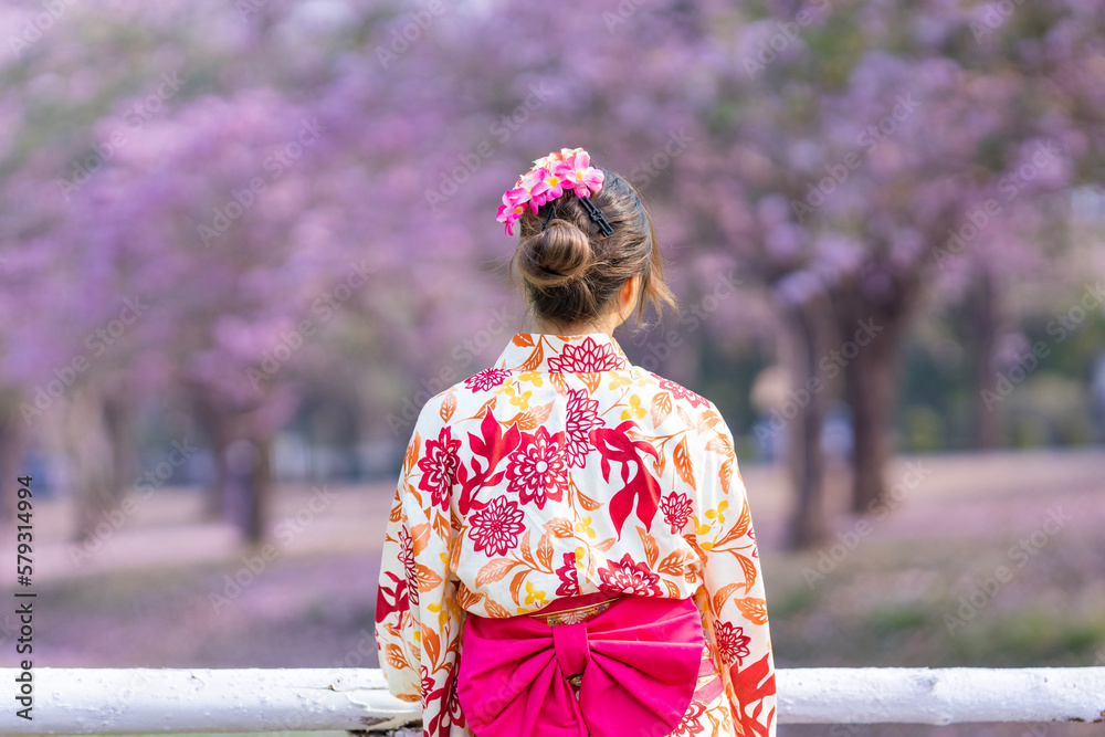 The back of Japanese woman in traditional kimono dress is looking at the view of sakura flower tree in the park at cherry blossom spring festival with copy space