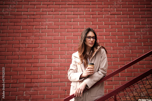 A casual woman standing outdoors on stairs and enjoying coffee to go.