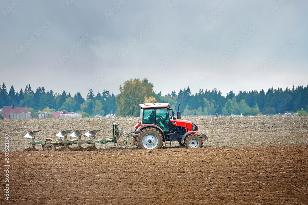 Obraz premium Tractor cultivating field. Tractor plowing soil on farm field. Tractor harrow plowing soil, rural landscape background. Soil cultivation, farm life. Сountryside landscape.