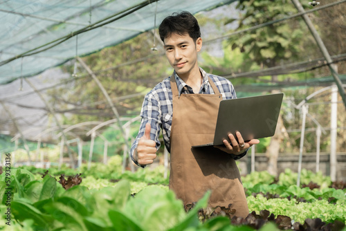 Farmer with laptop computer checking quality and freshness of organic vegetables hydroponic.