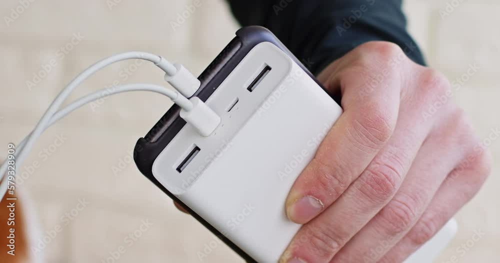 Person plugs mobile phone to powerbank on light background closeup. Man uses portable battery to charge smartphone. Power equipment Person plugs mobile phone to powerbank on light background closeup. Man uses portable battery to charge smartphone. Power equipment