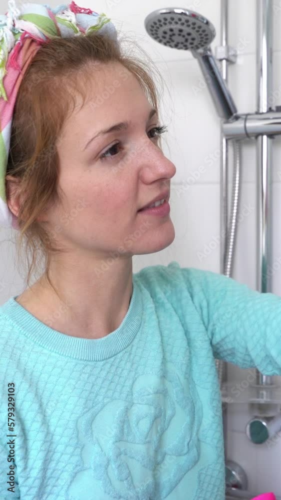 Woman with a rubber glove cleans a shower stall in the bathroom using means for cleaning and smiles at the camera. Vertical video Woman with a rubber glove cleans a shower stall in the bathroom using means for cleaning and smiles at the camera. Vertical video