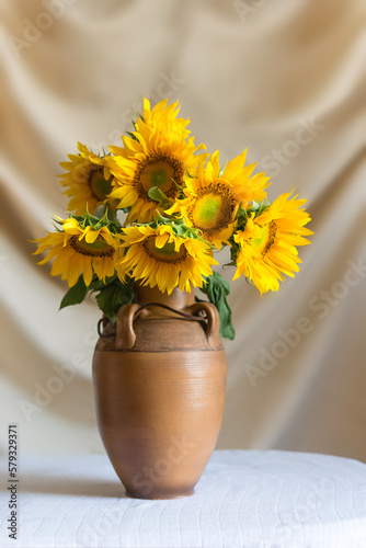 Still life with beautiful sunflowers in a clay ceramic vase on the table against the backdrop of light curtains