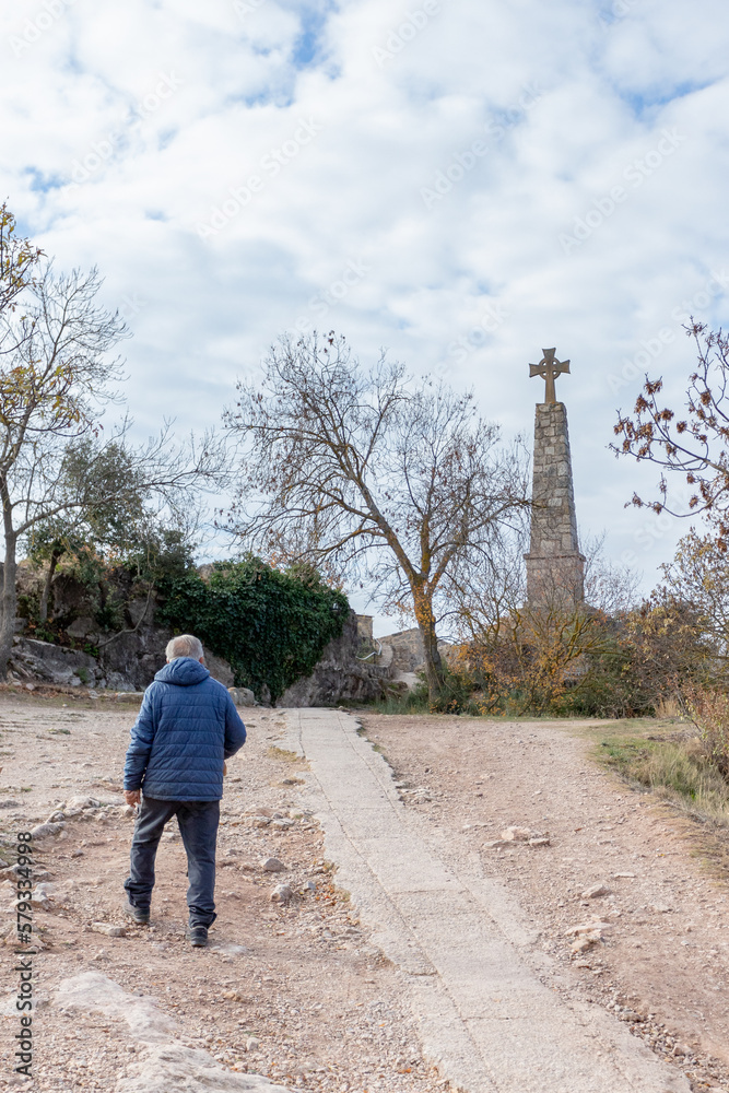 Older man walking towards the stone cross.