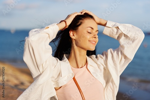 A girl with her eyes closed in the sun against the ocean smile with teeth, flying hair, tanned skin, rest, the concept of skin care in summer and spring.
