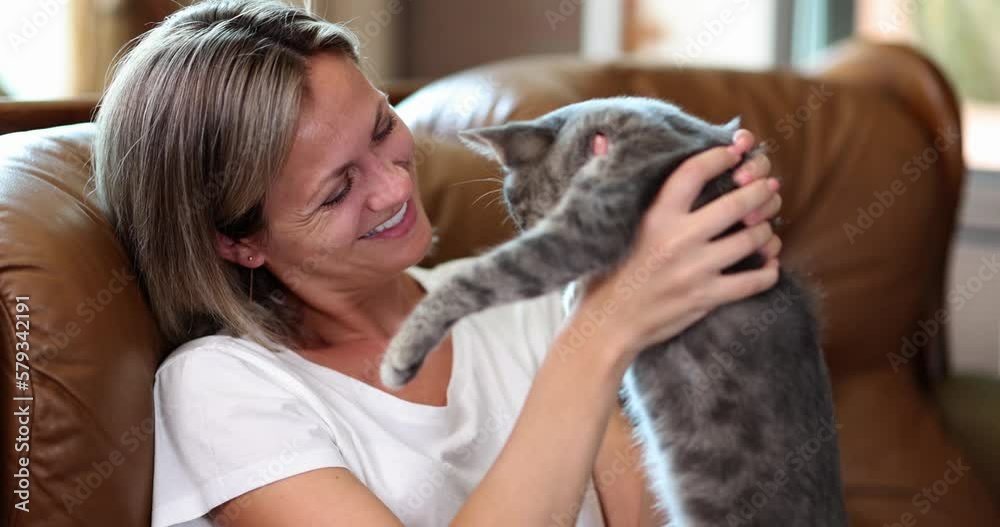 Smiling happy female sits on sofa with gray cat
