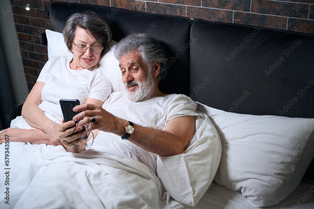 Old couple resting in bed, watching movie