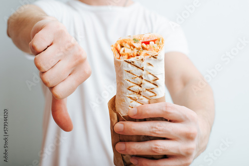 Close-up of caucasian man holding shawarma, kebab or doner and showing judgmental negative dislike gesture. Bad tasteless harmful fast food