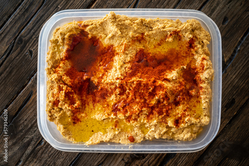 Home-made hummus in a plastic container with paprika and oil-