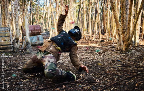 Man, paintball and dodging shots in the matrix for intense battle or war in the forest on knees. Male paintballer or soldier ducking to dodge paint balls in extreme adrenaline sports outdoors photo