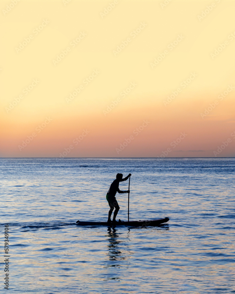 Silhouette of man is rowing on a SUP board against background of sunset sky. Standing paddleboarding