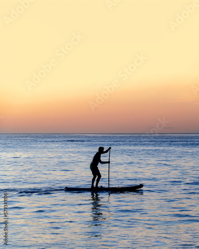 Silhouette of man is rowing on a SUP board against background of sunset sky. Standing paddleboarding © Ninaveter