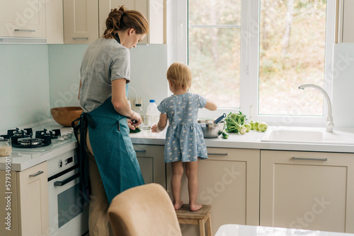 Obraz na plátně View from the back of a mother with a little daughter cooking in the home kitchen