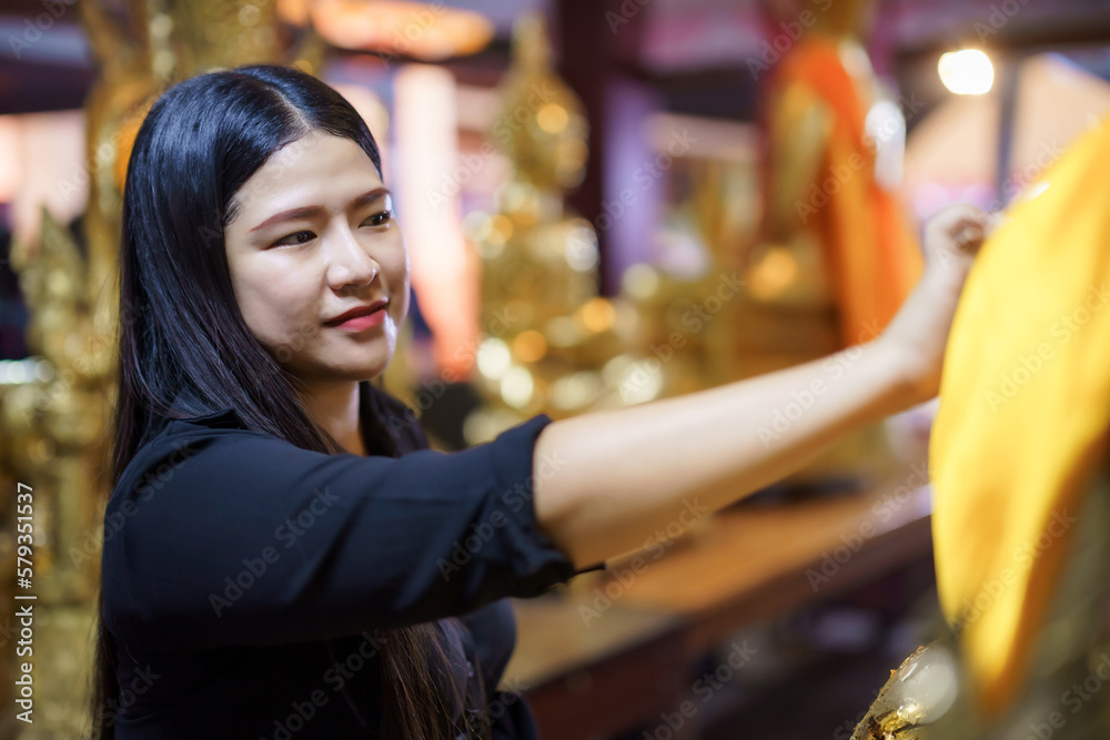 asian woman tourist Gilding gold leaf to Buddha for worship with faith to Buddha statue in temple thailand belief in Buddhism