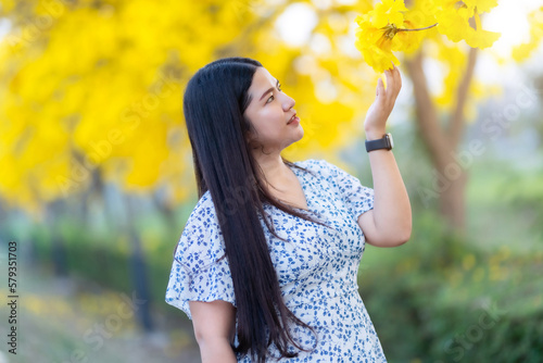 Happy Relaxing Portrait asian woman in Beautiful blooming Yellow Golden Tabebuia Chrysotricha flowers with the park in spring day at Evening background in Thailand.