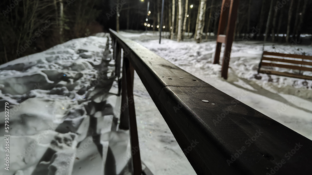Long black railings of fence on a winter night and white snow all around. Partial focus and distant blur