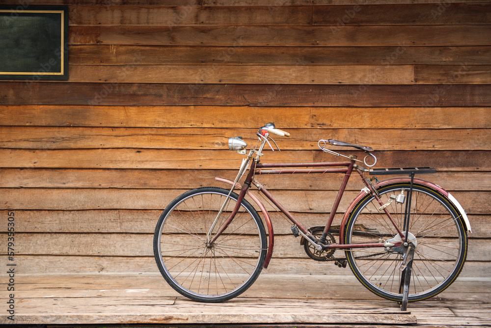 Vintage bicycle on old rustic dirty wall house, many stain on wood wall. Classic bike old bicycle on decay brick wall retro style. Cement loft partition and window background.