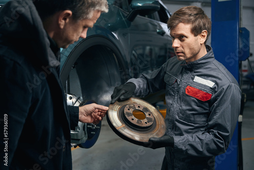 Portrait of repairman holding brake disc, talking with client