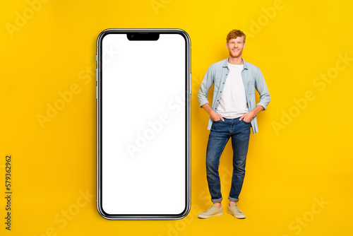 Photo of positive confident man wear jeans shirt arms hands pockets modern gadget empty space isolated yellow color background