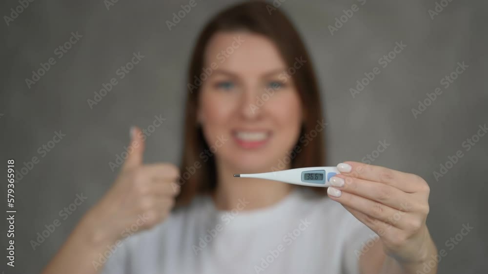 Woman holds an electronic thermometer in her hands, showing 36.6 degrees Celsius Woman holds an electronic thermometer in her hands, showing 36.6 degrees Celsius