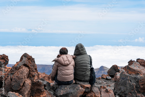pareja observando el paisaje sentados en montaña rocosa con ropa de invierno