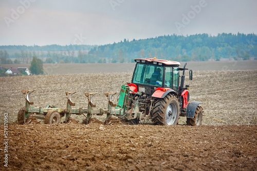 Tractor cultivating field. Tractor plowing soil on farm field. Tractor harrow plowing soil, rural landscape background. Soil cultivation, farm life. Сountryside landscape.
