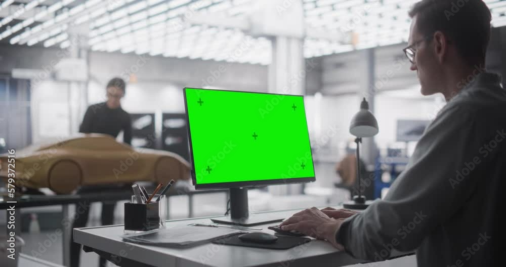 Automotive Designer Working on a Desktop Computer with Green Screen Mock Up Display. Digital Artist Creating a Concept Vehicle in a Studio. Modeler Working on Clay Model in the Background Automotive Designer Working on a Desktop Computer with Green Screen Mock Up Display. Digital Artist Creating a Concept Vehicle in a Studio. Modeler Working on Clay Model in the Background
