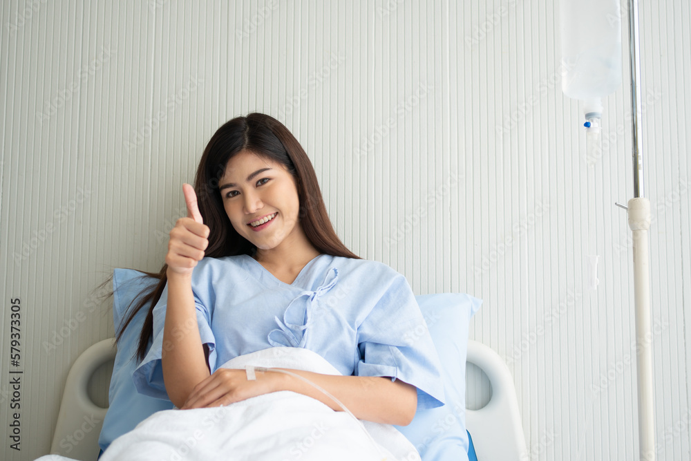 Happy Asian female patient smiling, lies on the bed, and raises thumb up to show confidence in treatment. Concept of believe in treatment And insurance coverage Happy Asian female patient smiling, lies on the bed, and raises thumb up to show confidence in treatment. Concept of believe in treatment And insurance coverage