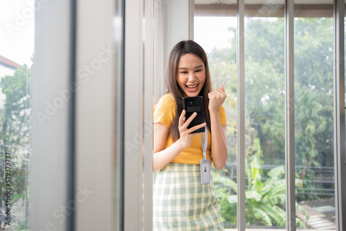 Happy young Asian women startup entrepreneur happy and excited smiling after getting message for success sign business contact  happy girl on workplace. Distance learning online education and work.