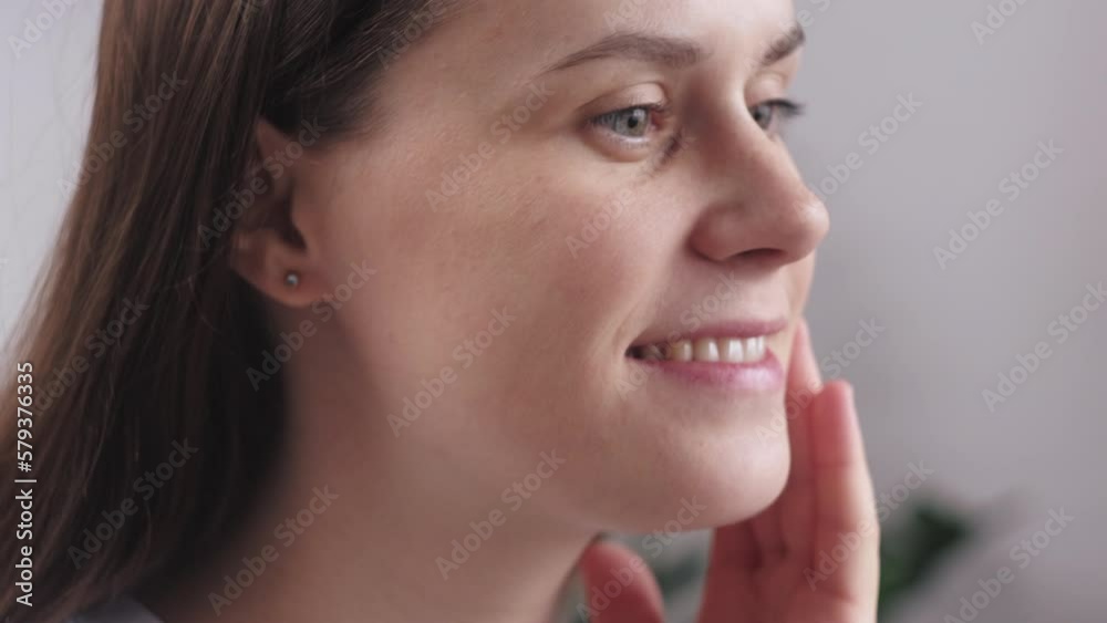 Close up portrait of happy attractive young female touching pretty face after applying cream do make up looking in mirror. Enjoy process smiles caring about perfect skin. Skincare and medical product Close up portrait of happy attractive young female touching pretty face after applying cream do make up looking in mirror. Enjoy process smiles caring about perfect skin. Skincare and medical product