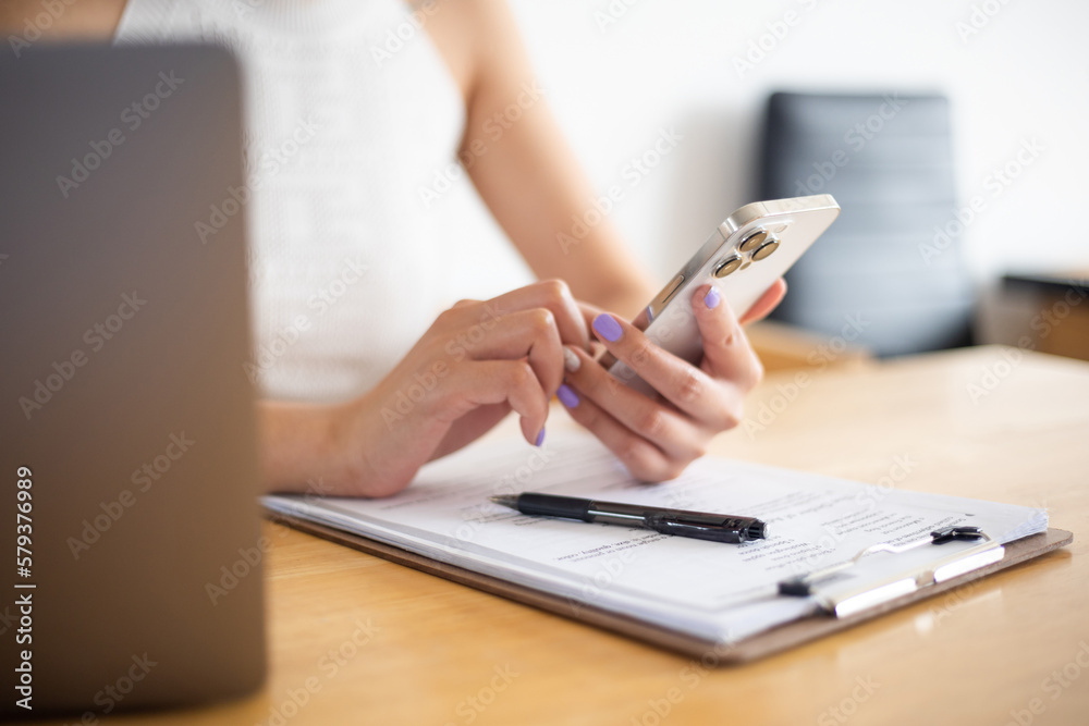 Fototapeta premium Close-up shot of beautiful young woman working with laptop and phone with documents on table at home