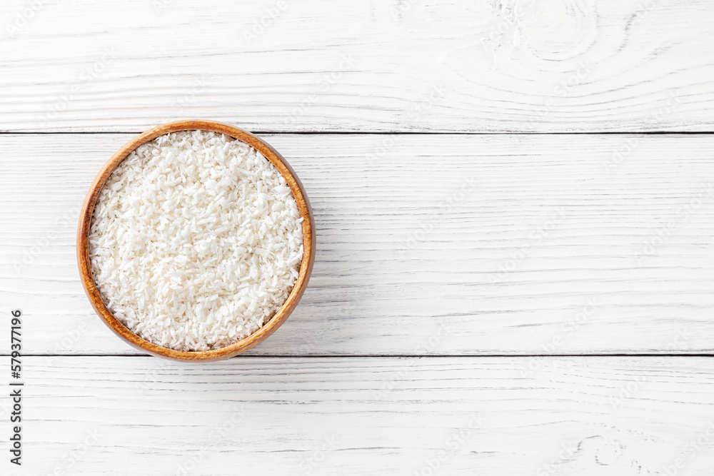 Coconut flakes in wooden bowl with scoop on white wooden background with copy space