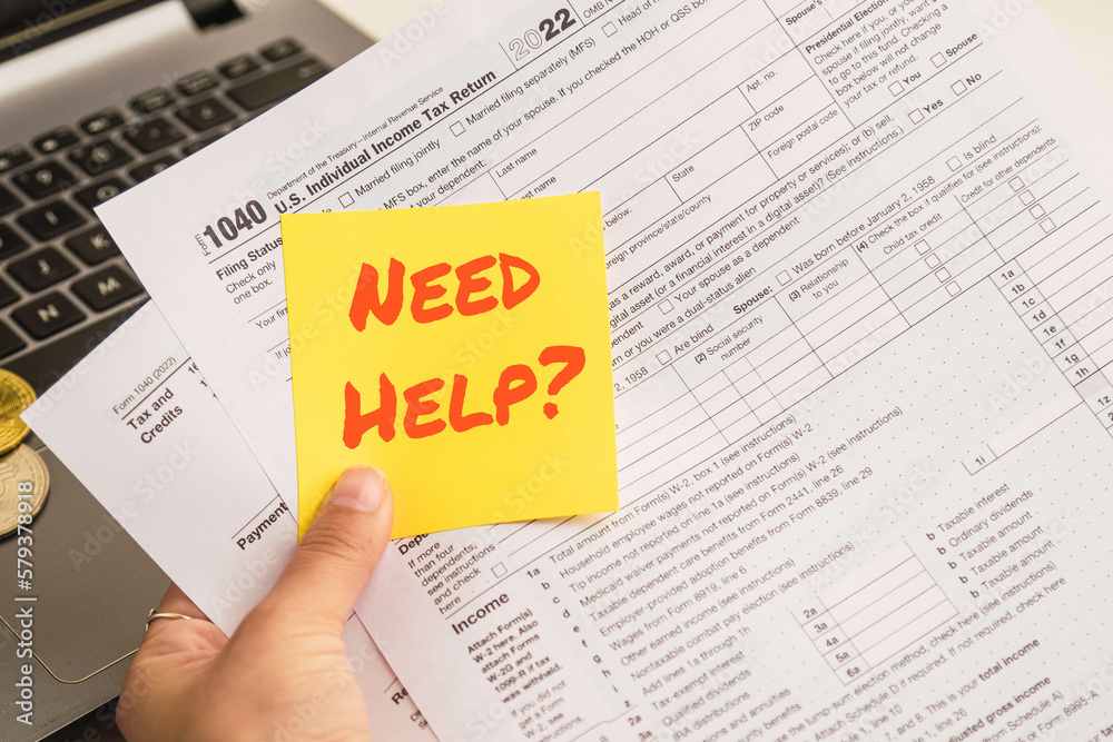 Obraz premium Hands holding a help text in spanish on sticky notes with 1040 tax forms , United States tax form, a laptop on a desk near some bitcoins. US individual income tax return. 