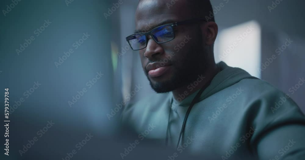 Close Up Portrait of Black Man Working on Computer, Lines of Code Language Reflecting on his Glasses. Male Programmer Developing New Software, Managing Cybersecurity Project. Slow Motion Close Up Portrait of Black Man Working on Computer, Lines of Code Language Reflecting on his Glasses. Male Programmer Developing New Software, Managing Cybersecurity Project. Slow Motion