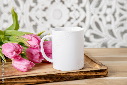 Selective focus on single one white mug mock up. Cup on home table with decorative spring flowers on background and bohemian style wood panel. Cozy seasonal products advertisement background.