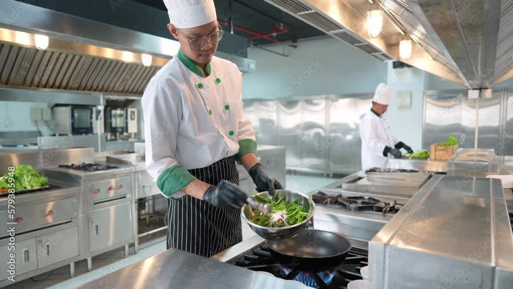 Asian male chef stir frying food in a wok at the kitchen.