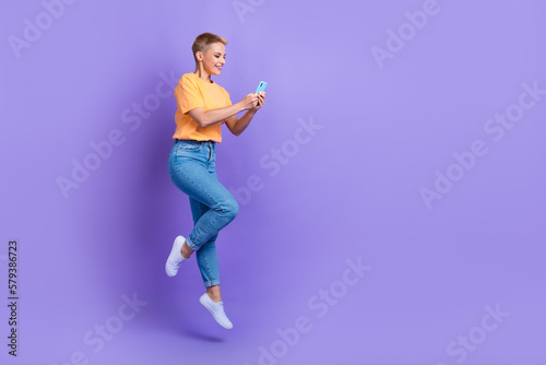Full body profile portrait of carefree energetic lady jump use smart phone empty space isolated on purple color background © deagreez